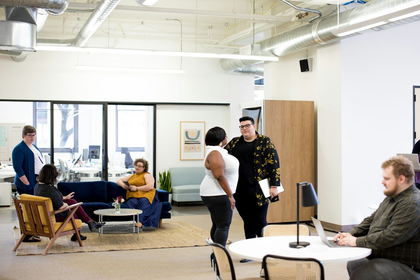Team members talking in a modern open office while a colleague works on a laptop